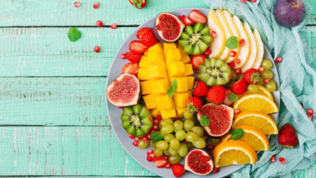 A colorful fruit dish with mango, kiwi, figs, strawberries, grapes, and orange slices is arranged on a gray plate, 4K Desktop Wallpaper
