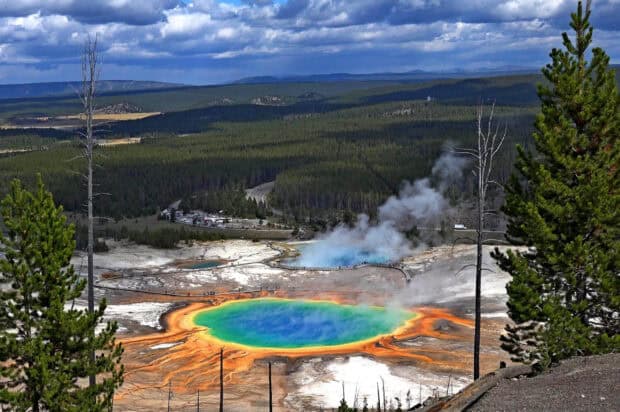 The colorful hot spring at Yellowstone National Park is surrounded by a forest and steaming geothermal features, 2K Desktop Wallpaper