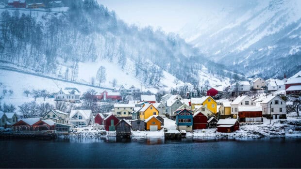 Colorful houses stand along the snowy shores of the Norwegian fjords under misty mountains, HD Desktop Wallpaper