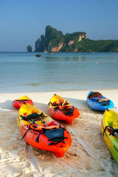 A group of colorful kayaks rests on the sandy shore with clear water and rocky islands in the background featuring Palawan Wallpapers, HD Mobile Wallpaper