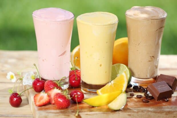 Three milkshake glasses with cherries, strawberries, citrus, and chocolate arranged on a wooden table, HD Desktop Wallpaper