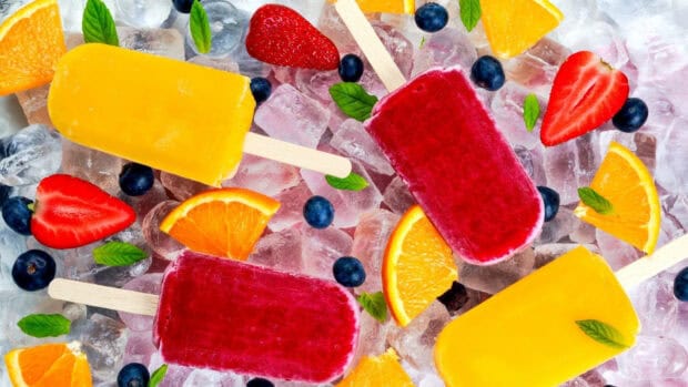 Red and yellow popsicles surrounded by strawberries and oranges on ice, HD Desktop Wallpaper
