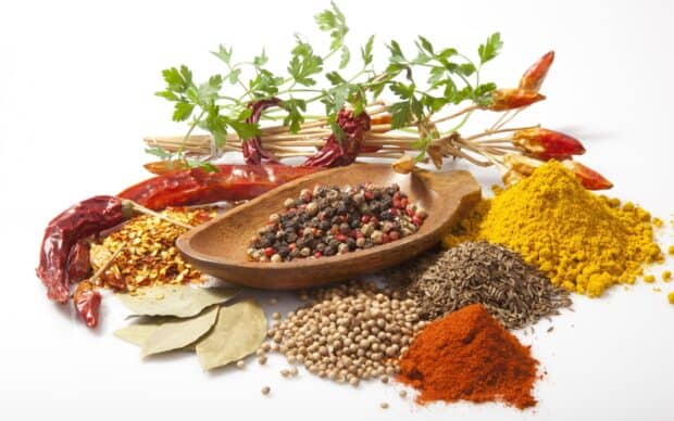 A wooden scoop holding mixed peppercorns surrounded by various seasoning spices and fresh herbs, 2K Desktop Wallpaper
