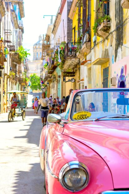 A pink vintage car parked on a vibrant street in Havana Cuba with people walking nearby, HD Mobile Wallpaper