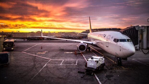 A commercial aircraft is parked at the airport gate with a vibrant sunset in the background, 4K Desktop Wallpaper