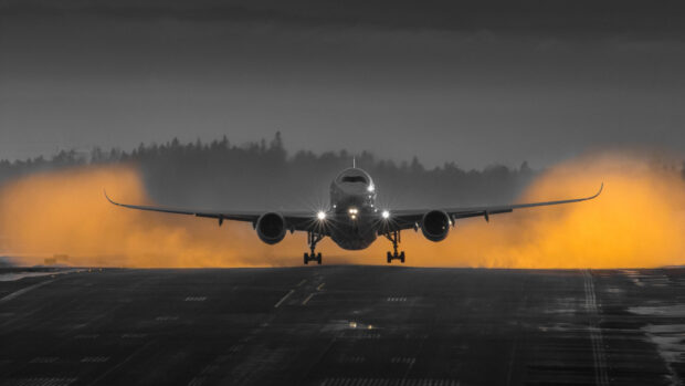 A commercial aircraft is landing on a runway with bright lights illuminating the scene and forest in the background, 4K Desktop Wallpaper