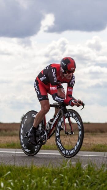 A cyclist in Bmc gear races on a road under a cloudy sky, HD Phone Wallpaper