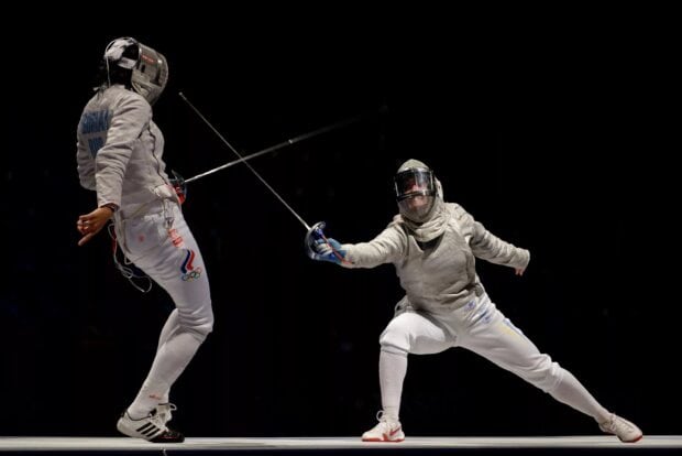 Two skilled fencers engage in a match wearing full protective gear with swords, 2K Desktop Wallpaper