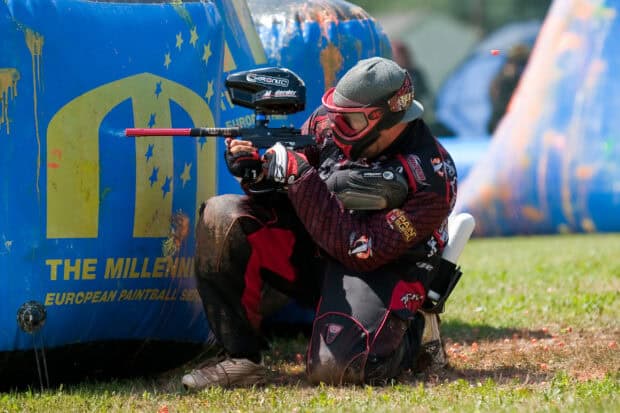 A paintball player is aiming his marker while crouching behind a bunker on the field, HD Desktop Wallpaper