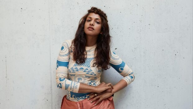 A confident Mia rapper poses in a patterned top against a concrete wall, HD Desktop Wallpaper