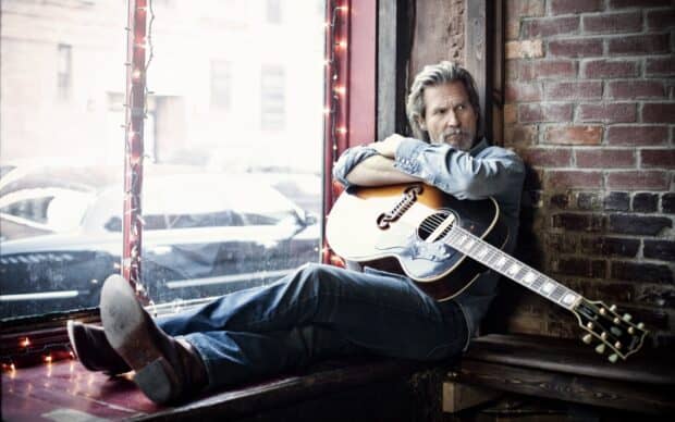 A man with a guitar sits thoughtfully by a window with brick walls in the background, HD Desktop Wallpaper