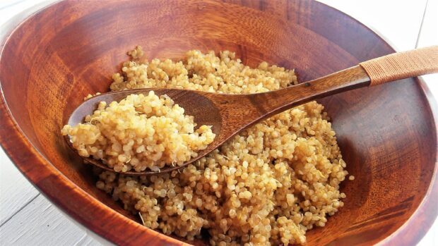 A wooden spoon holding cooked quinoa grains in a wooden bowl on a white surface, 2K Desktop Wallpaper