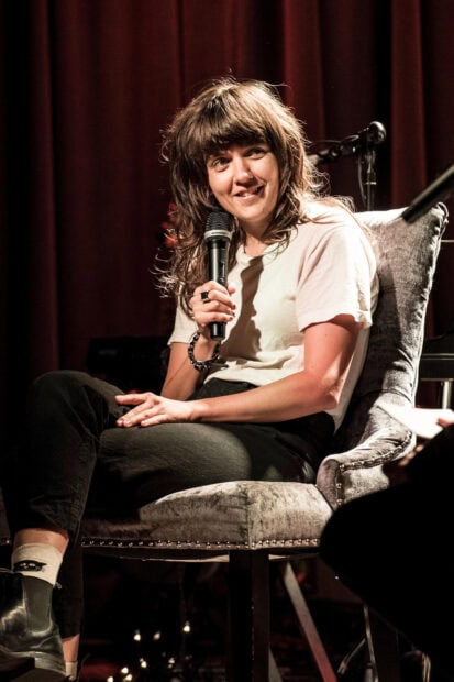 Courtney Barnett speaking into a microphone while seated during an event, HD Desktop Wallpaper