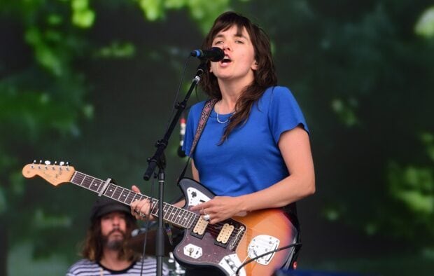 Courtney Barnett performs on stage playing guitar and singing in front of a green background, HD Desktop Wallpaper