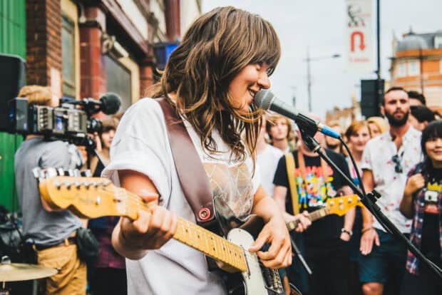 Courtney Barnett is playing guitar and singing in front of a crowd at an outdoor event, HD Desktop Wallpaper