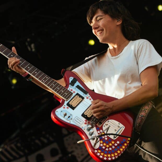 Courtney Barnett smiles while playing an electric guitar decorated with stars during a live performance, HD Desktop Wallpaper