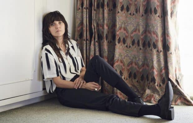 A woman wearing striped shirt and black pants sits on the floor by decorative curtains in a relaxed pose, HD Desktop Wallpaper