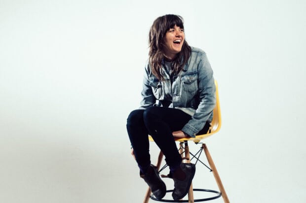Courtney Barnett is sitting and laughing on a yellow chair wearing a denim jacket, 2K Desktop Wallpaper