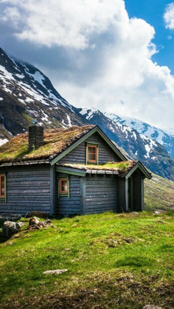 A cozy cabin with a grass roof sits in the Norwegian mountains under a cloudy sky, 2K Phone Wallpaper