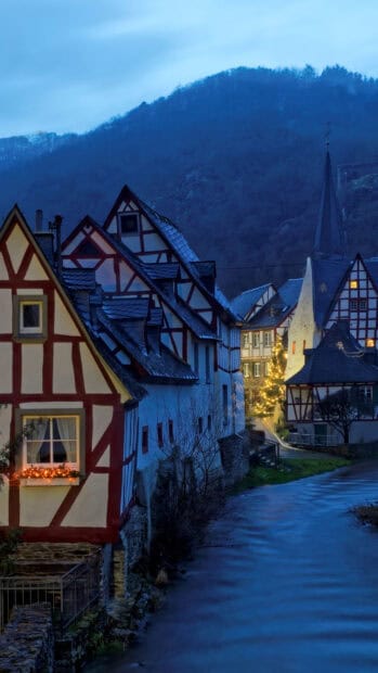 A peaceful village with traditional houses and glowing lights by the water under a dark blue sky, HD Phone Wallpaper