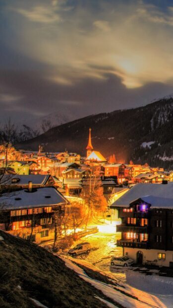 A cozy winter village glows warmly under snow and dark mountains, HD Phone Wallpaper