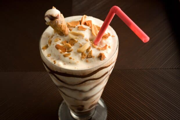 A creamy milkshake with chocolate swirls topped with crushed nuts and a small ice cream cone, 2K Desktop Wallpaper