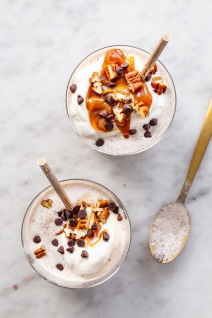 Two glasses of milkshake topped with caramel, nuts, and chocolate chips on a marble table, HD Mobile Wallpaper