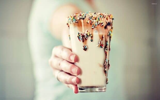 A hand holding a creamy milkshake topped with chocolate and colorful sprinkles, HD Desktop Wallpaper