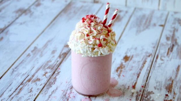 A creamy pink milkshake topped with whipped cream and red sprinkles on a wooden surface, HD Desktop Wallpaper