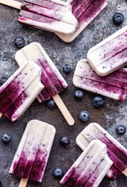 Creamy popsicle with blueberry flavor surrounded by fresh blueberries on a rustic surface, HD Mobile Wallpaper