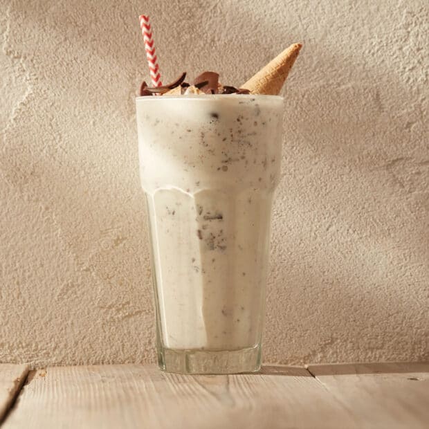 A creamy vanilla milkshake topped with chocolate pieces and a waffle cone on a wooden table, HD Mobile Wallpaper