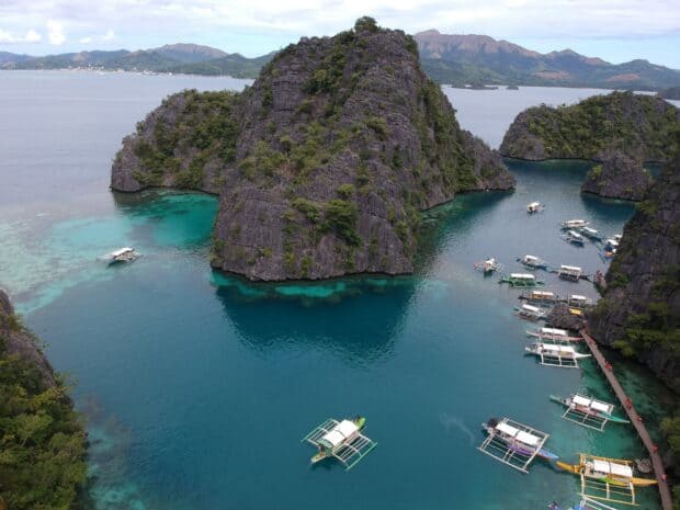 This Palawan Wallpapers image shows turquoise waters surrounding limestone cliffs and boats, HD Desktop Wallpaper