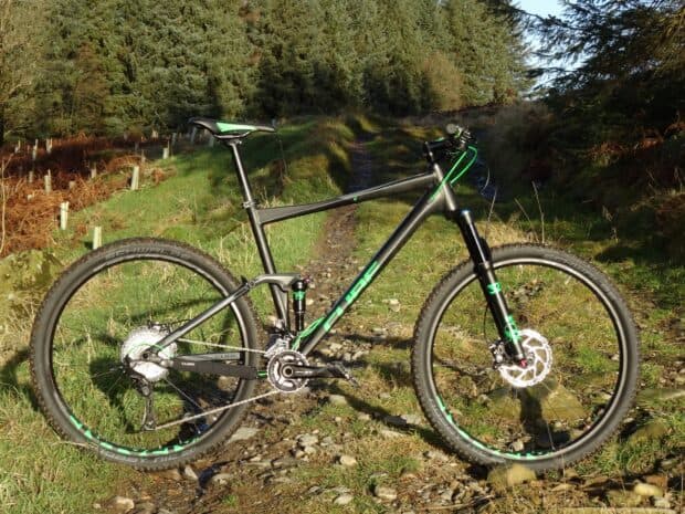 A Cube bike is parked on a rocky forest trail surrounded by trees and grass, HD Desktop Wallpaper