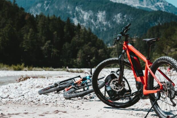A red Cube bike stands on rocky ground with forested mountains in the background, 2K Desktop Wallpaper