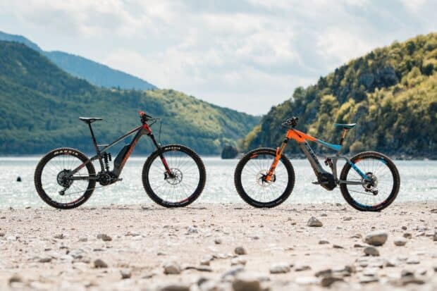 Two Cube bikes are standing on rocky shore near lake with mountains in the background, HD Desktop Wallpaper