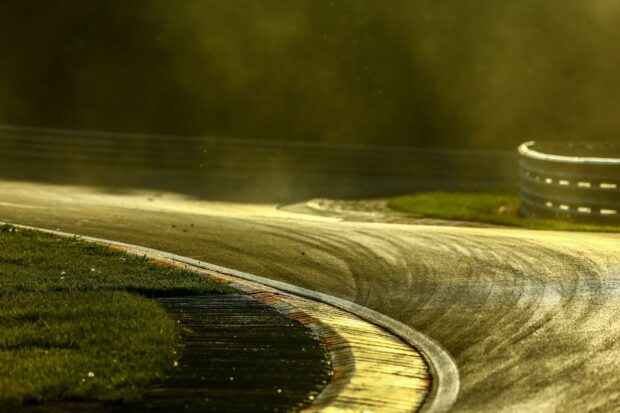 A curved section of a race track shines under golden light with visible tire marks and guardrails, HD Desktop Wallpaper