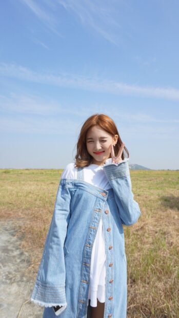 A cheerful Nayeon smiles and poses with a peace sign outdoors in a sunny field, HD Phone Wallpaper