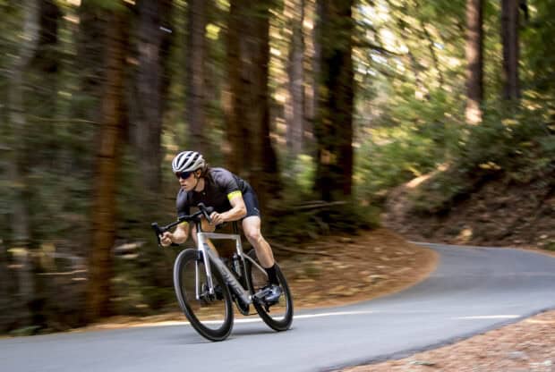 A cyclist wearing a helmet rides a Bmc bike through a wooded trail during the day, HD Desktop Wallpaper