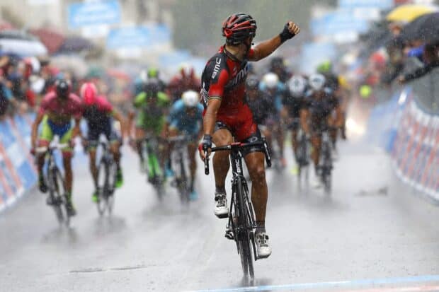 A cyclist wearing a Bmc kit celebrates a win during a rainy race, 2K Desktop Wallpaper