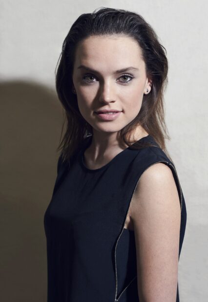 Daisy Ridley smiles wearing a black sleeveless top in soft lighting, 2K Phone Wallpaper