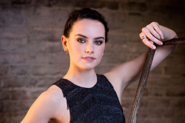 Daisy Ridley poses confidently wearing an elegant black dress in front of a brick wall, HD Desktop Wallpaper