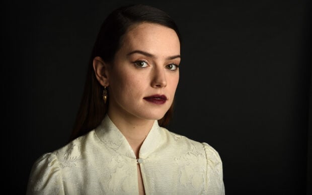 The portrait shows Daisy Ridley with dark lipstick and a cream textured blouse against a black background, 2K Desktop Wallpaper