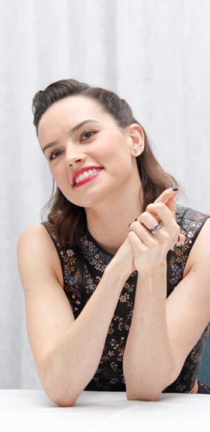 Daisy Ridley is smiling gently while sitting at a table in a floral dress, 2K Phone Wallpaper