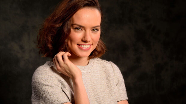 Daisy Ridley smiles warmly while posing in a textured top against a dark background, 4K Desktop Wallpaper