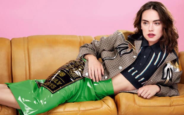 Daisy Ridley is posing on a yellow sofa wearing a colorful outfit with a pink background, 2K Desktop Wallpaper