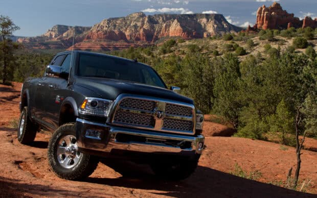 A dark gray Ram pickup truck is parked on a rugged terrain with trees and rocky hills in the background, 2K Desktop Wallpaper