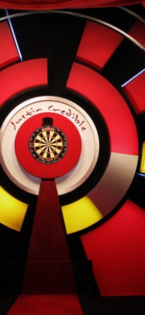 A darts board with red and yellow target rings is displayed in a dark room, HD Phone Wallpaper