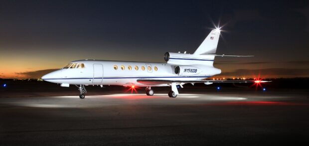 A Dassault Falcon 50 jet is parked on the runway at dusk with its lights on, 2K Desktop Wallpaper