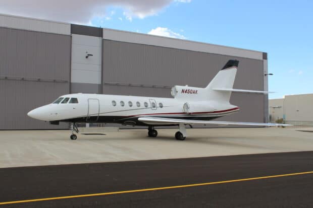 A Dassault Falcon 50 parked on an airport tarmac in front of hangars under a partly cloudy sky, 2K Desktop Wallpaper