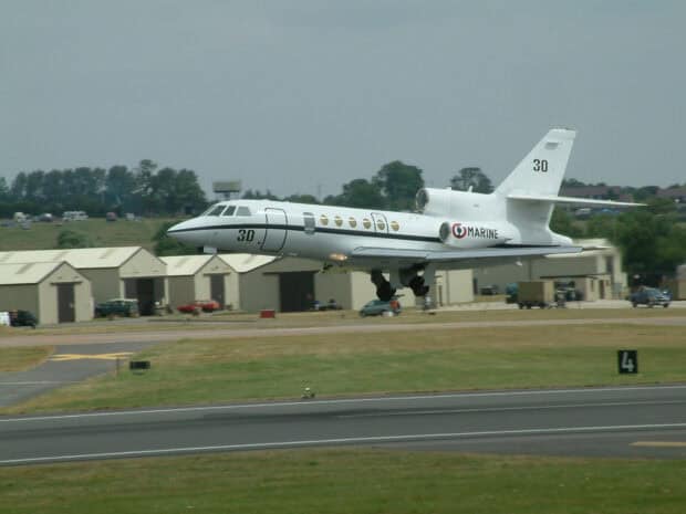 A Dassault Falcon 50 is captured while landing on a runway near hangars and vehicles, HD Desktop Wallpaper